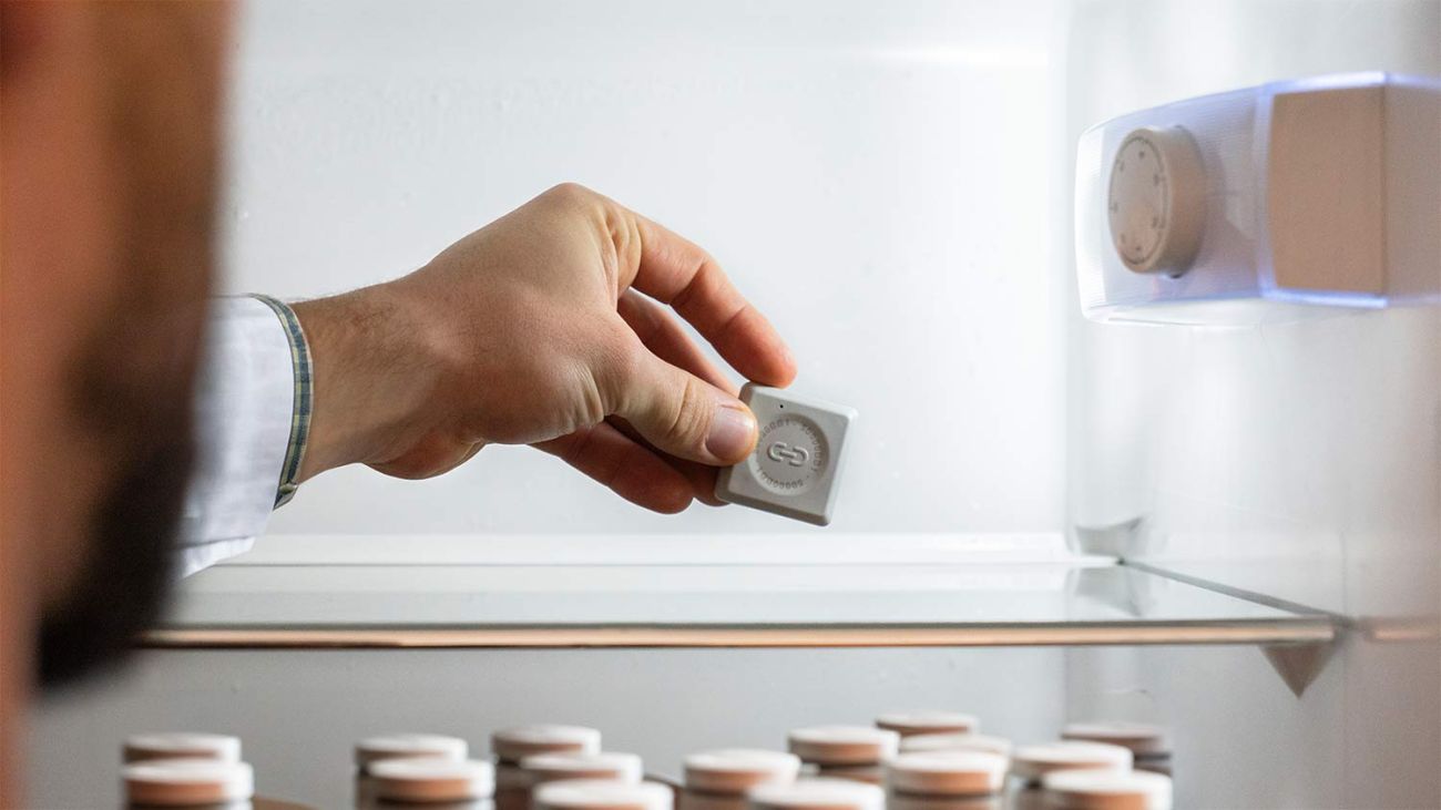 Das Bild zeigt eine Person, welche einen Sensor in einen geöffneten Medikamenten Kühlschrank einlegt.